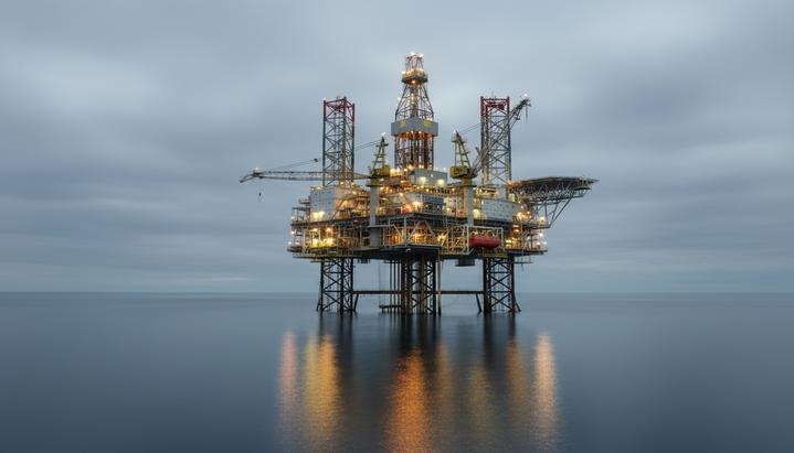 Самоподъемная морская буровая установка с опущенными опорами стоит в открытом море. На палубе видны краны и буровая вышка.