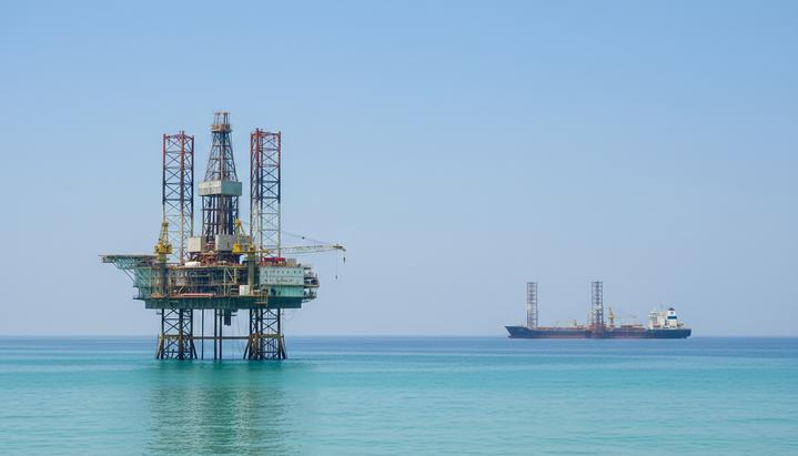 Самоподъемная морская буровая установка в море у побережья. На горизонте видны добывающая платформа и судно-нефтехранилище.